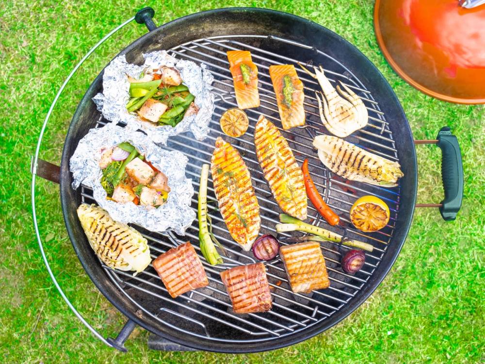 Grill med ulike fiskestykker, skalldyr og grønnsaker på en gressplen, klar for servering.