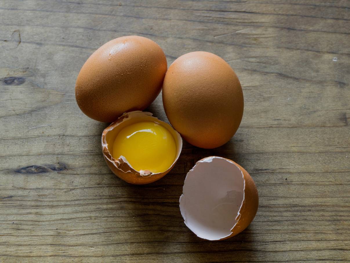 To hele egg og ett halvt egg med sprukket skall og innhold på en treverkebakgrunn