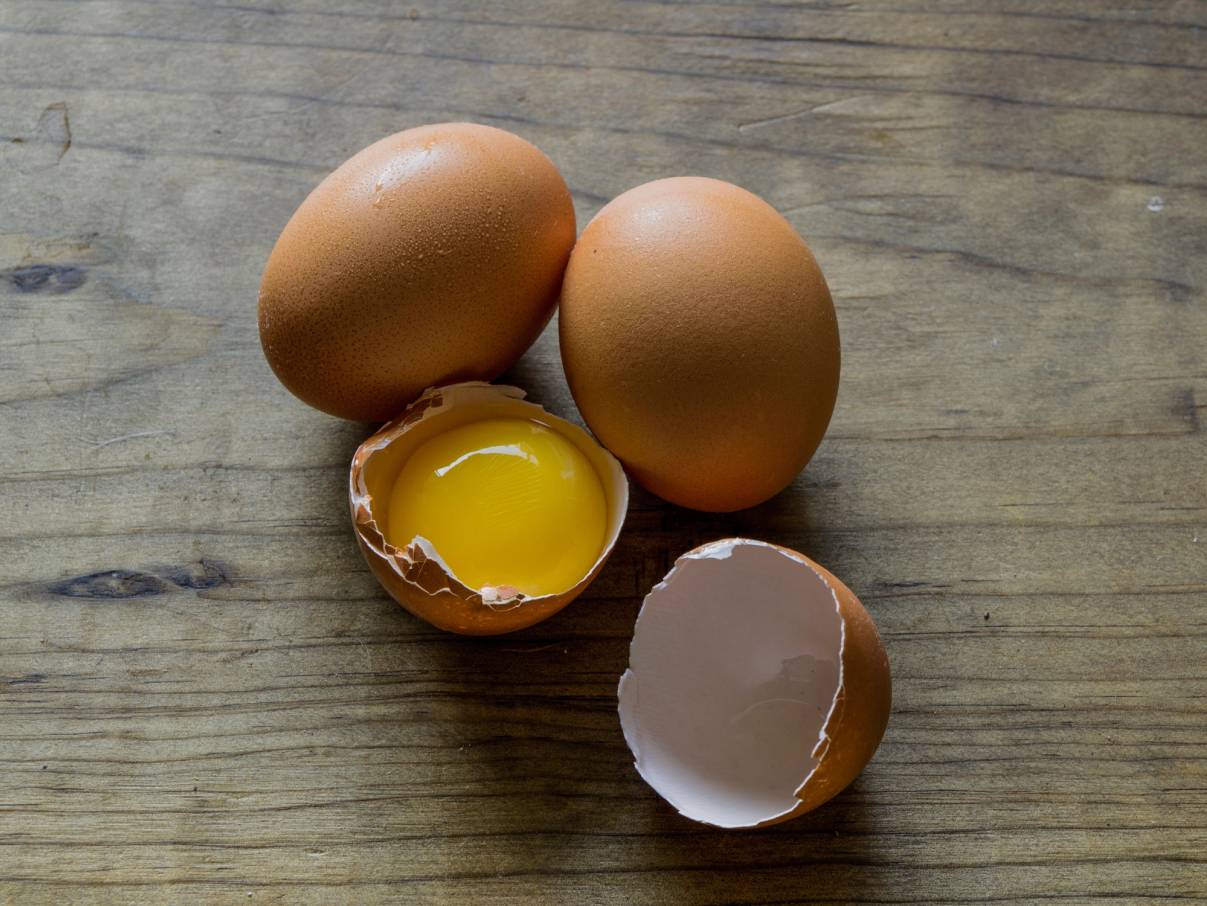To hele egg og ett halvt egg med sprukket skall og innhold på en treverkebakgrunn