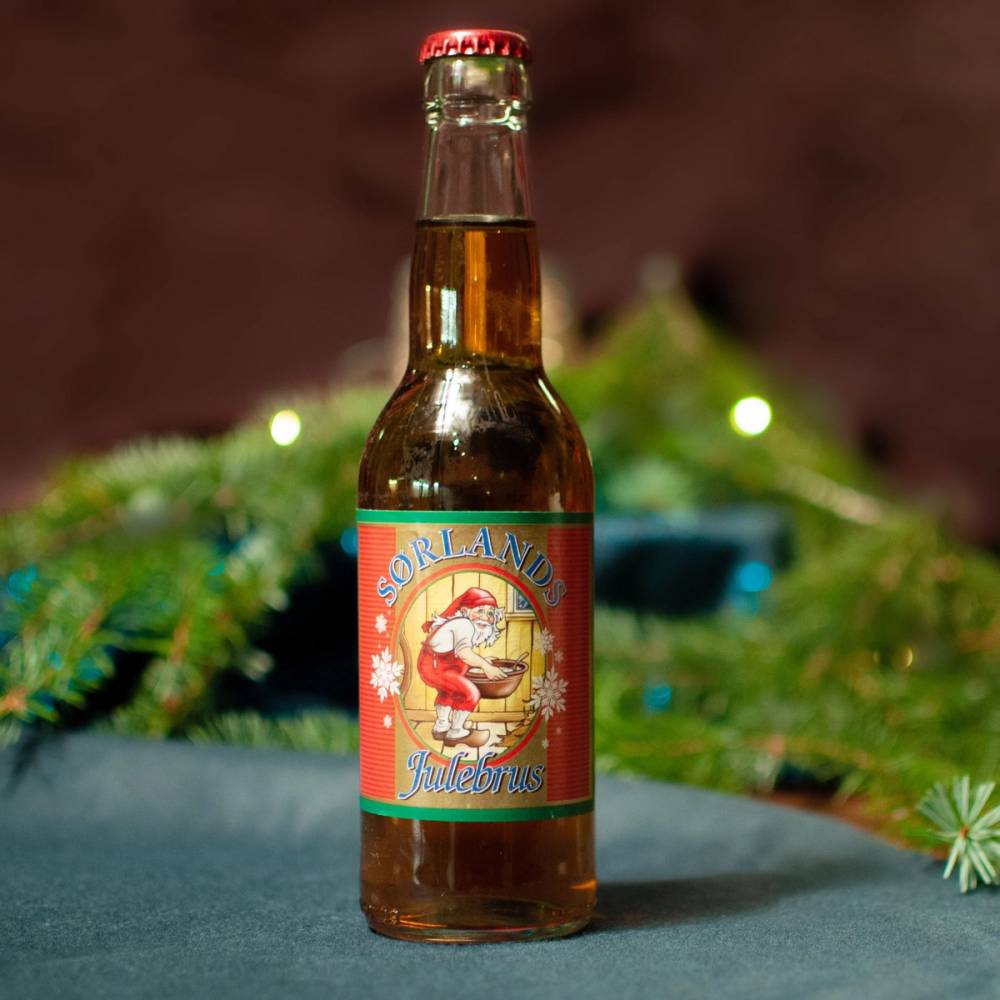 En flaske Sørlandet julebrus med jule- og vinterdekor i bakgrunnen.
