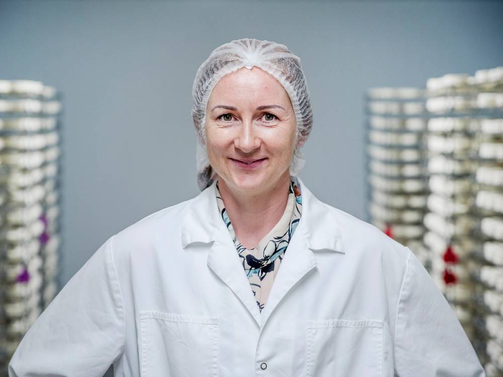Meierisjef Dovre Sigrid Svanborg iført hvit labfrakk i et meieri, med hyller fylt med meieriprodukter i bakgrunnen.