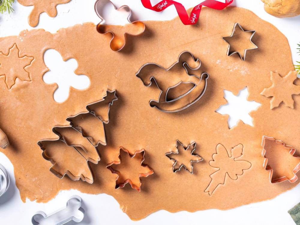 Ulike pepperkakeformer og utstikkere på et kjevle med pepperkakedeig, klare til å lage pepperkaker.