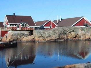 To røde hus med hvite detaljer ligger ved vannet på en steinrøys i Østfold, Norge.