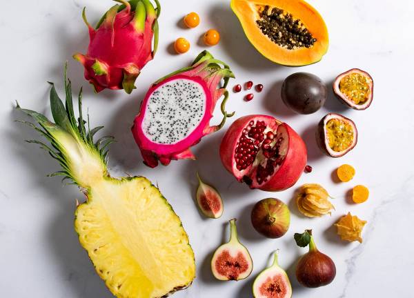 Et utvalg av eksotiske frukter, inkludert dragefrukt, ananas, pasjonsfrukt, granateple, og kiwifrukt, spredt ut på en hvit bakgrunn