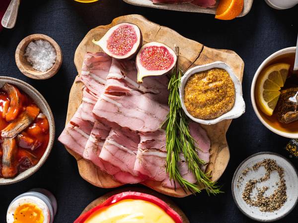 Et julefrokostbord med skinke, sennep, sitron, og diverse tilbehør på en svart duk.