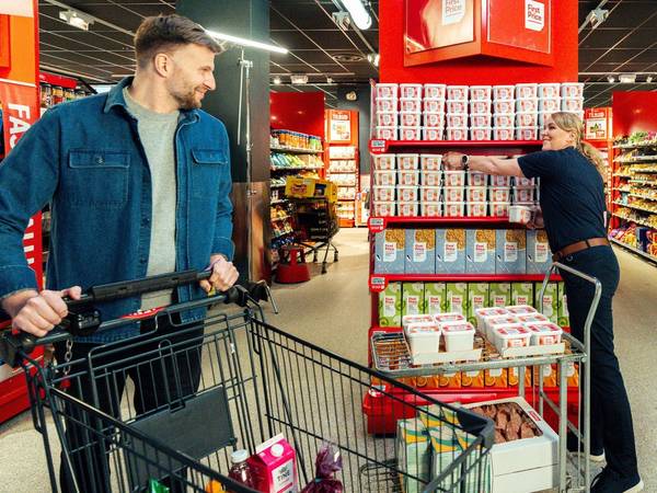 En matarbeider fyller opp hyller med First Price-produkter i en dagligvarebutikk.