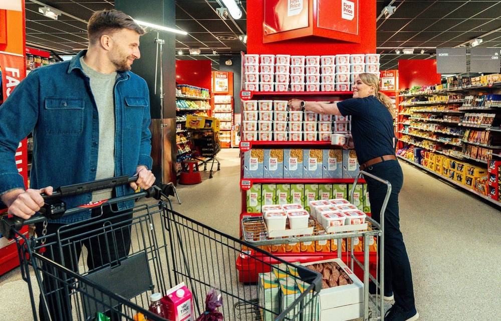 En matarbeider fyller opp hyller med First Price-produkter i en dagligvarebutikk.