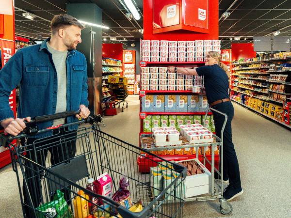 En matarbeider fyller opp hyller med First Price-produkter i en dagligvarebutikk.