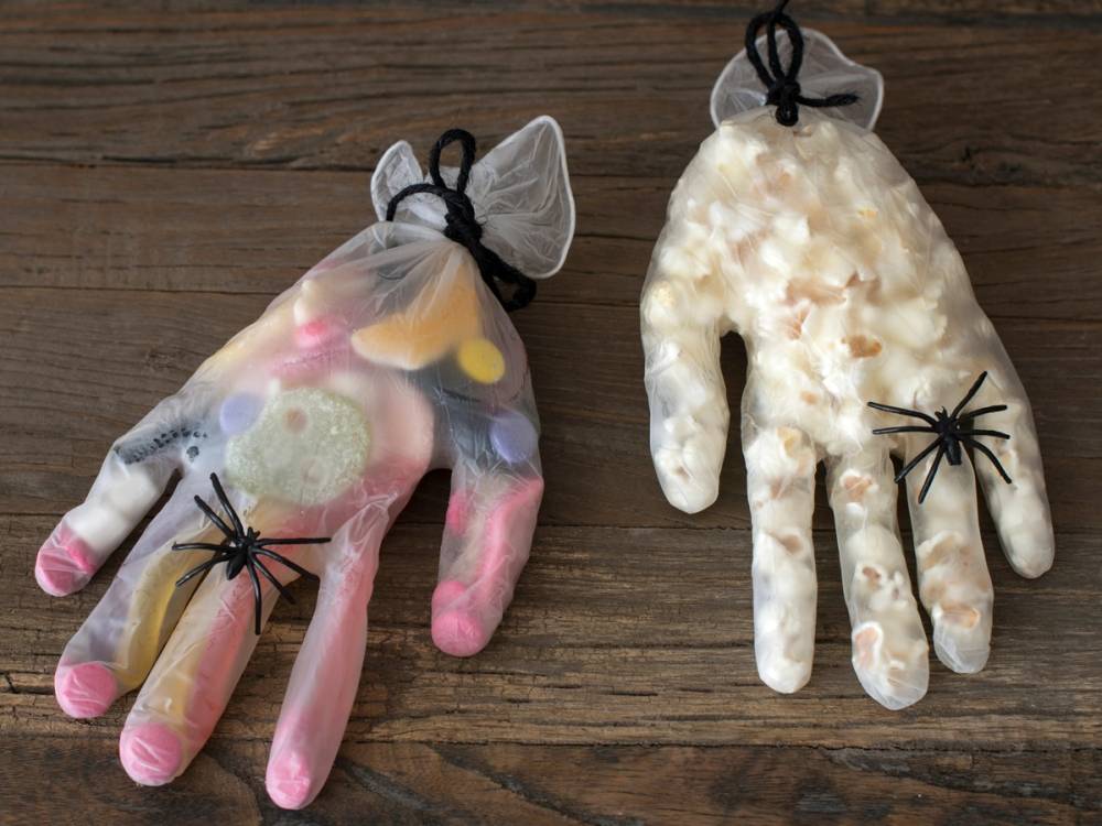 To hånddukker formet som hender, en med fargerike materialer og en med hvite bomullsdotter, ligger på en treoverflate, begge med svarte edderkopper på seg.