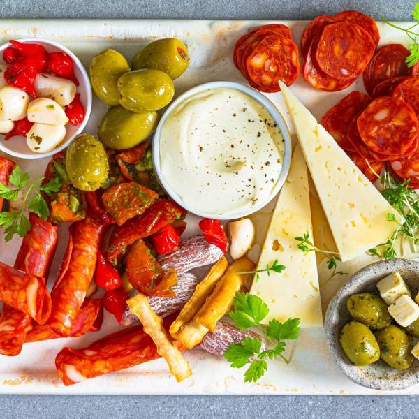 Et fat med ulike typer tapas, inkludert oliven, cherrytomater, ost, og spekepølser, pyntet med frisk urter.