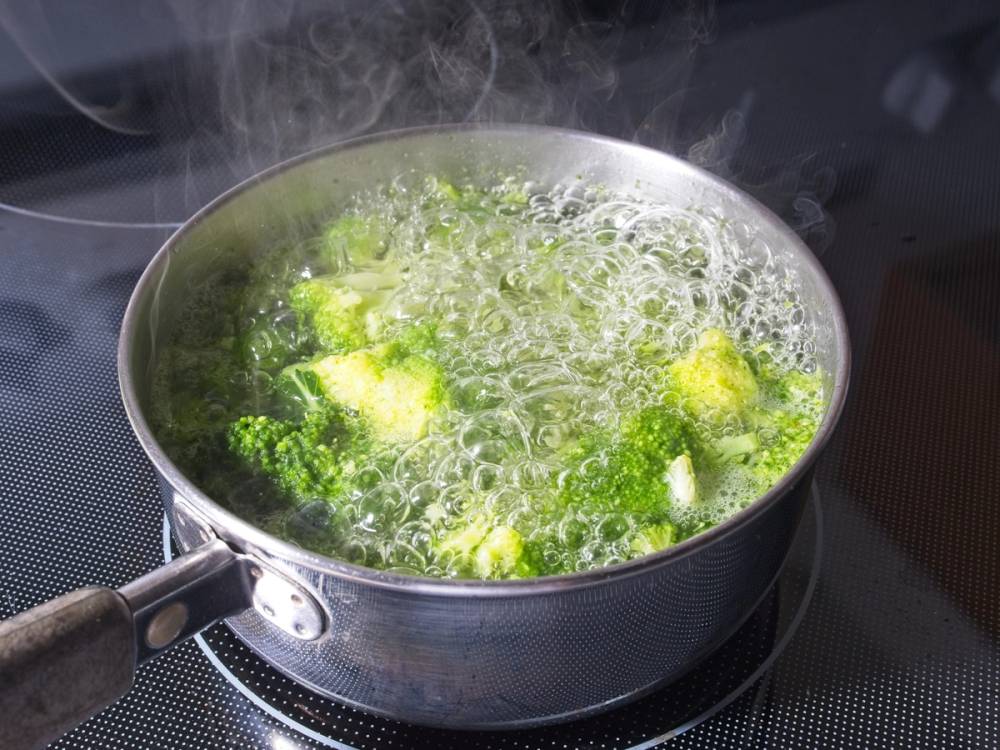 Brokkoli koker i en gryte på komfyren med damp som stiger opp.