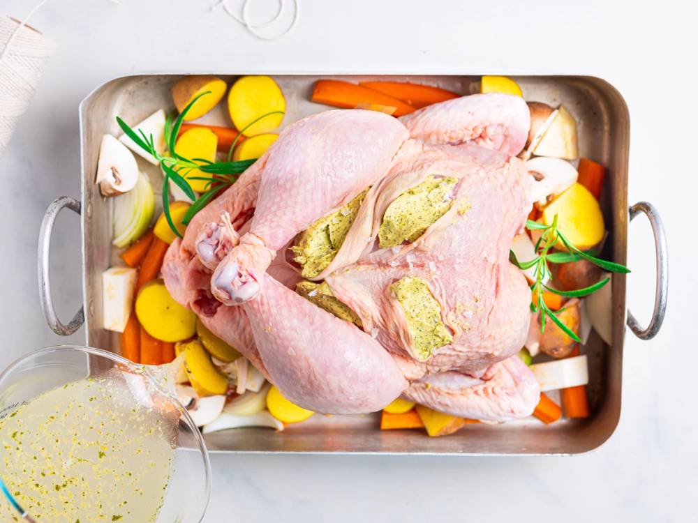 Helstekt kylling med urtesmør og grønnsaker i en ildfast form før steking.