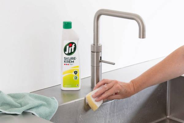 En person bruker en svamp til å vaske en kjøkkenbenk med Jif skurekrem, med en flaske av produktet på benken ved siden av.