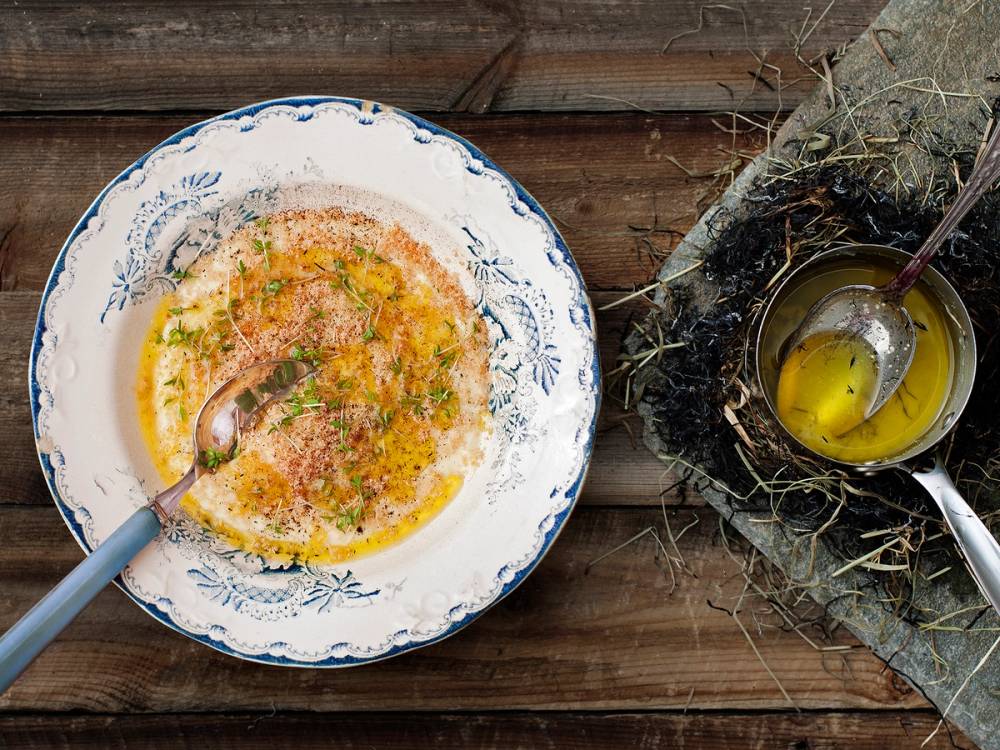 En bolle med en egg- og urterøre, og en kopp med et egg i en nest på et trebord, med en skje i koppen.