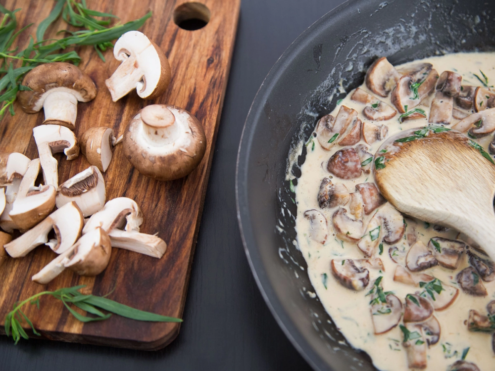 Skjære sopp på en skjærefjøl mens en soppstuing lages i en panne ved siden av.