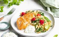 Kyllingfilet med blomkålris og friske bringebær på en hvit tallerken, omgitt av små boller med saus og en gaffel.