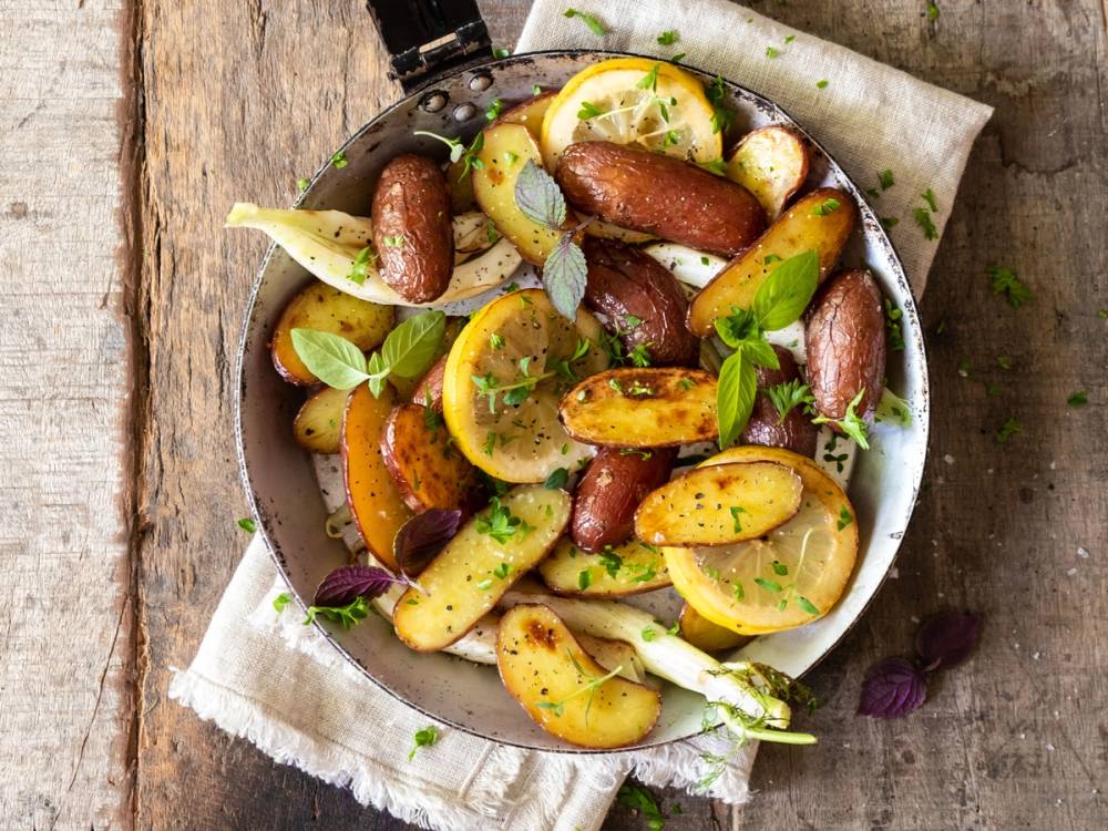 Ovnsbakte poteter med fennikel og sitron i en skål med friske urter, på et treverkebord.
