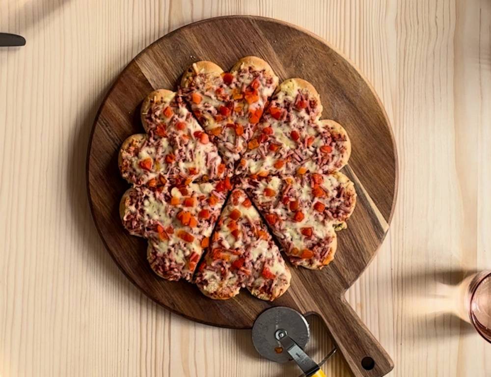 En hjerteformet pizza med ost og pepperoni på en rund treplate.