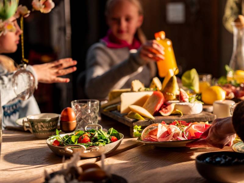 To personer som spiser og deler mat på et bord med ulike retter og drikke, i et innendørs miljø.