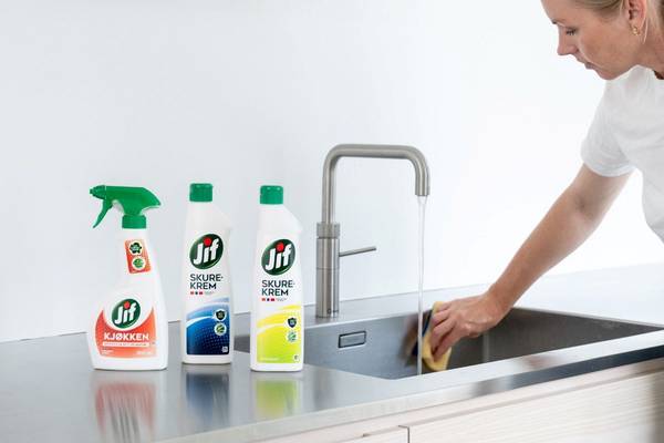 En person vasker opp i et kjøkken med Jif rengjøringsprodukter på benken.