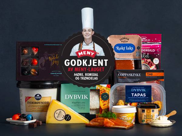 Et utvalg av matvarer og godteri på et bord, inkludert ost, sjokolade og kjeks, med en person i kokkeuniform i bakgrunnen.