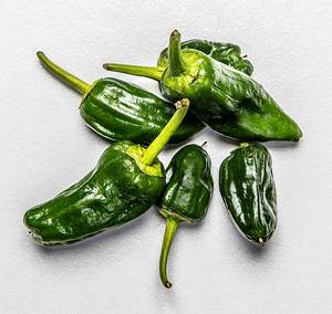 Fem grønne chilipepper av varierende størrelse ligger på en hvit bakgrunn.