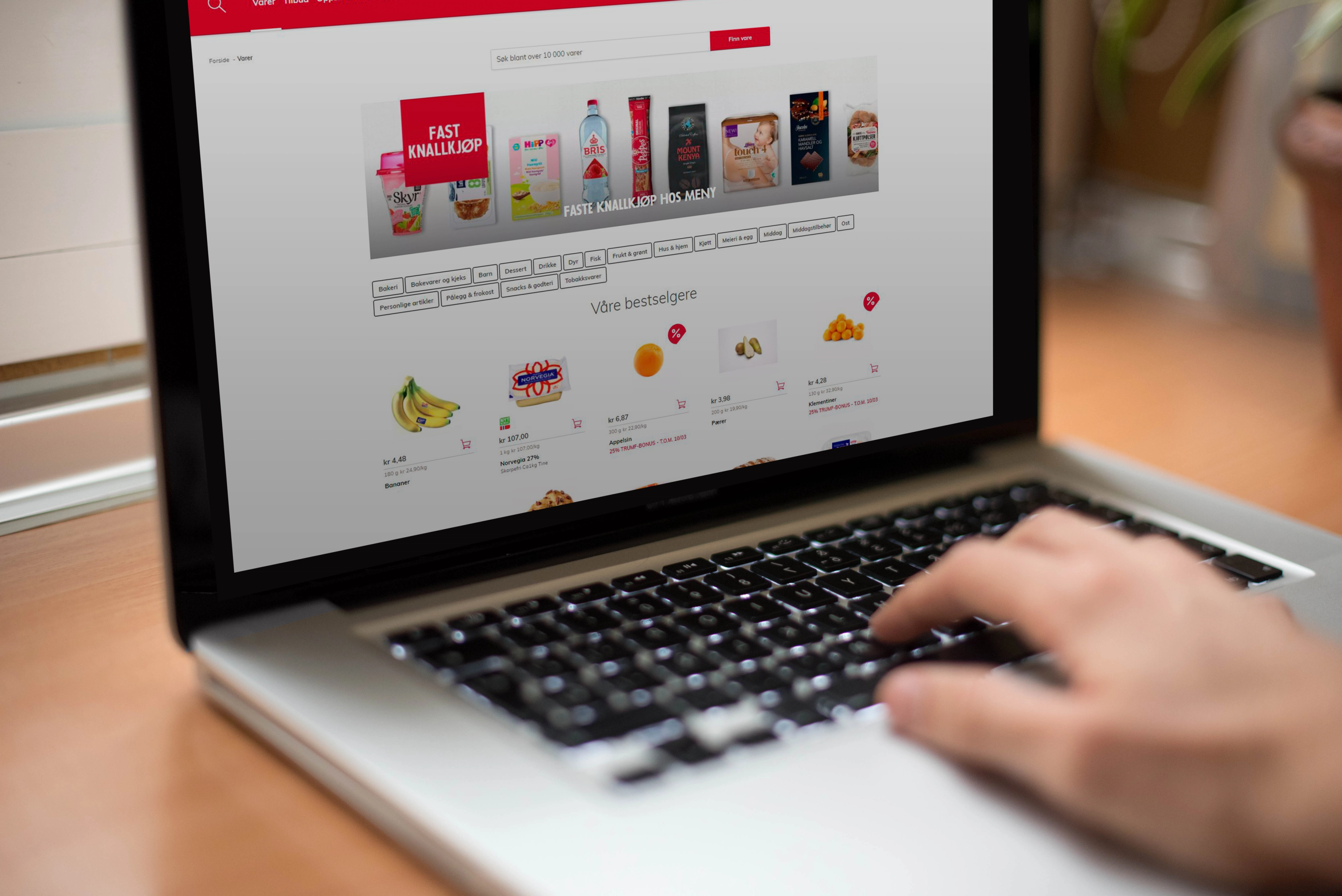 Nærbilde av en person som handler i en nettbutikk på en bærbar datamaskin, med produktbilder og bestillingsknapper på skjermen.