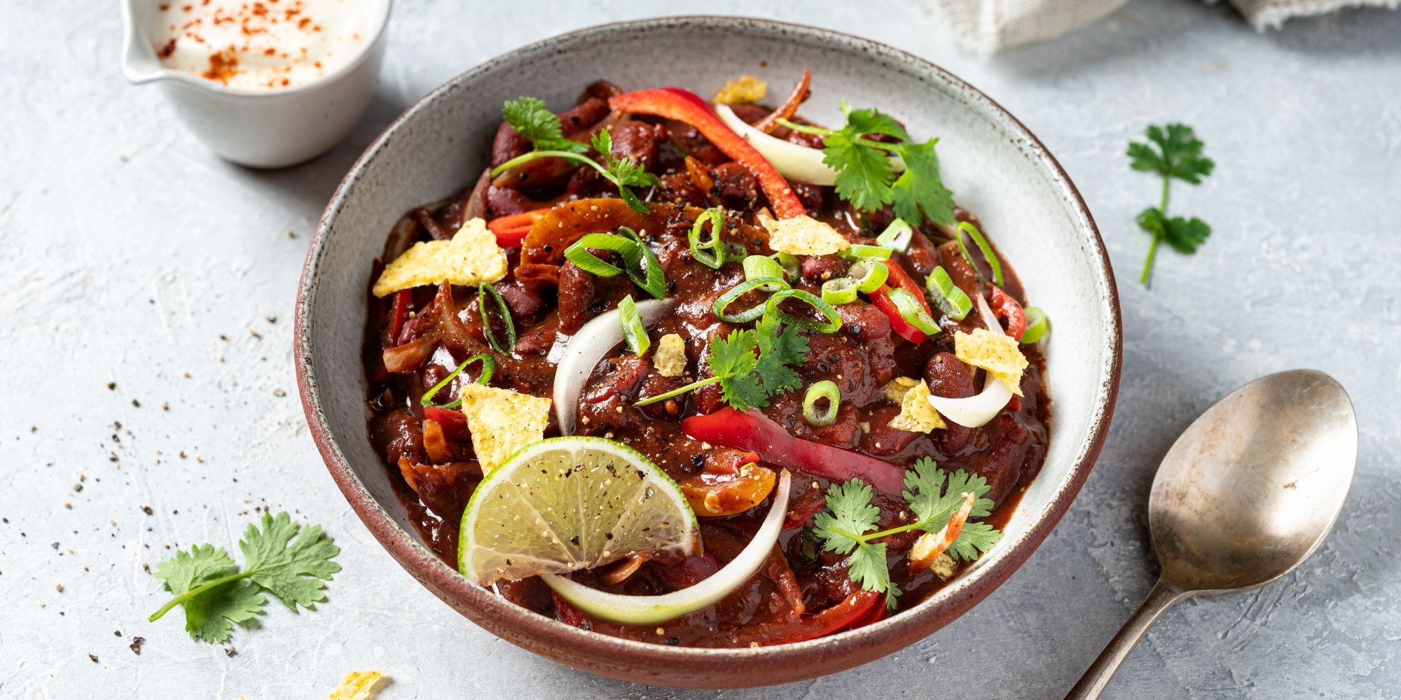 Chili sin carne i en bolle med limebåter, løk, koriander og grønnsaker, ser ut som en vegetarisk rett.