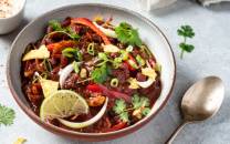 Chili sin carne i en bolle med limebåter, løk, koriander og grønnsaker, ser ut som en vegetarisk rett.