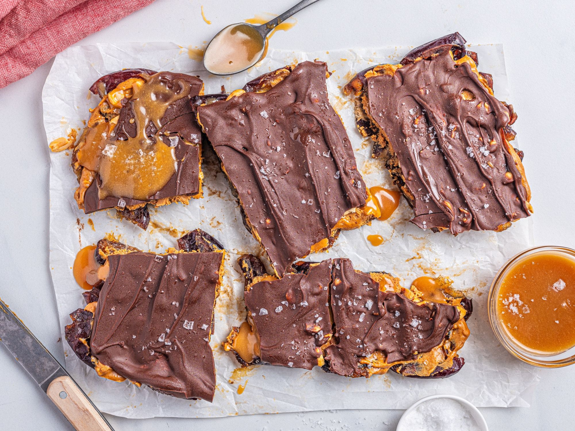 Knekkede og delte karamell- og sjokoladefylte kjeks med karamellsaus på siden, lagt på et hvitt papir på et bord.
