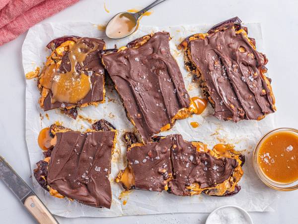 Knekkede og delte karamell- og sjokoladefylte kjeks med karamellsaus på siden, lagt på et hvitt papir på et bord.