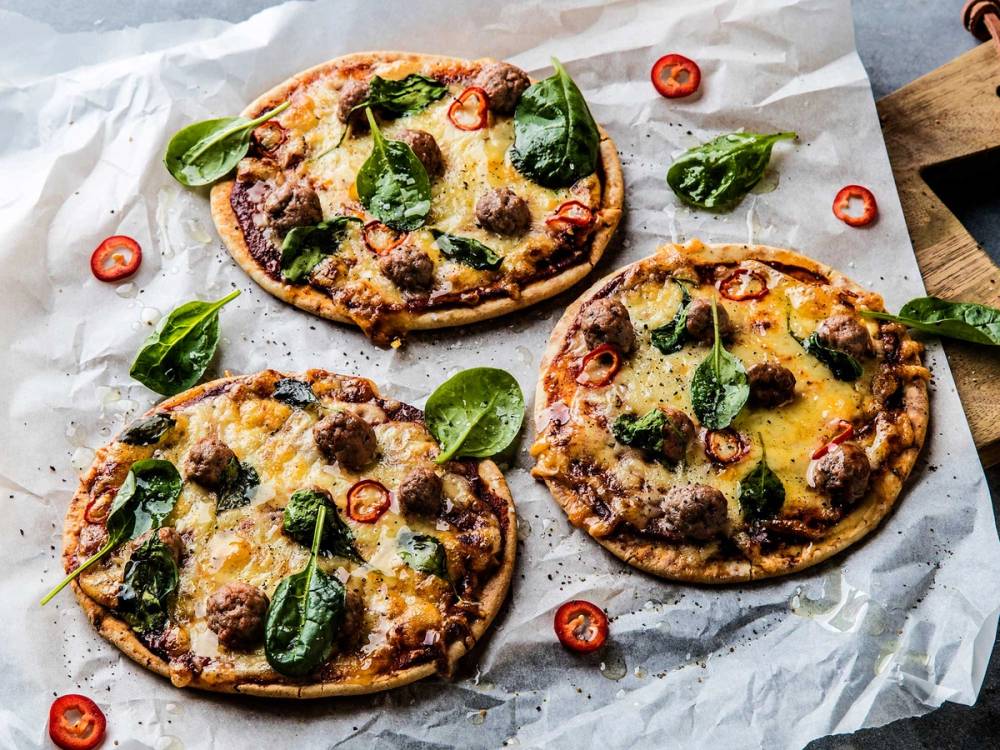 Tre små pizzaer med chorizo, spinat og cherrytomater på et hvitt papir, med noen skiver chili rundt.
