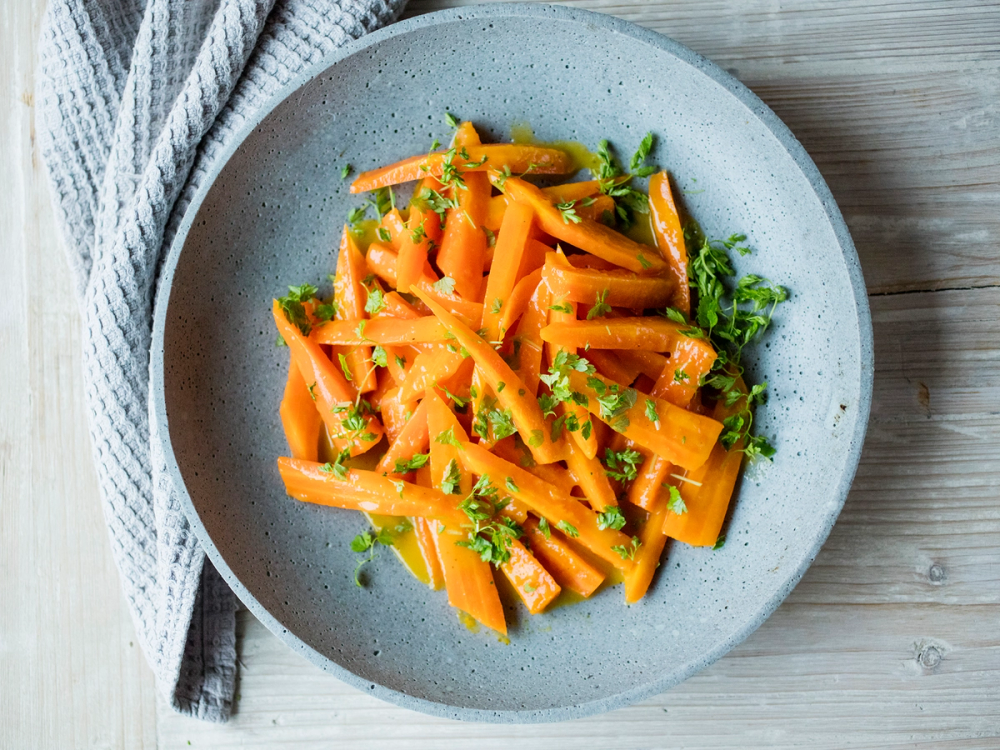 Appelsinkokte gulrøtter på en tallerken med hakket grønt på toppen.
