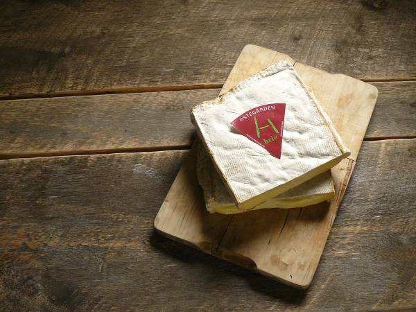 Et stykke ost med en rød og grønn etikett ligger på en skjærefjøl av tre på et trebord.