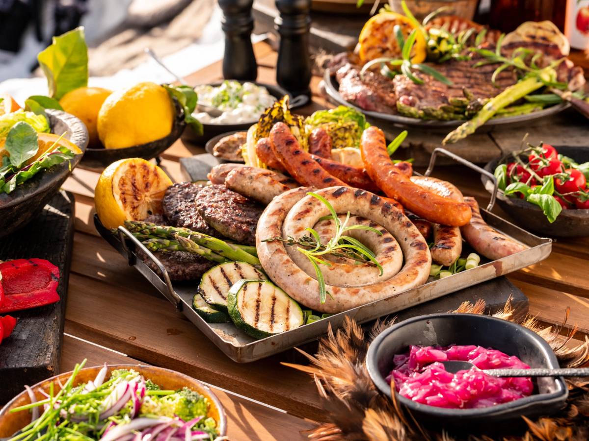 Et fat med ulike typer grillet kjøtt og grønnsaker, omgitt av sitroner og salater, på et bord dekket med mat.
