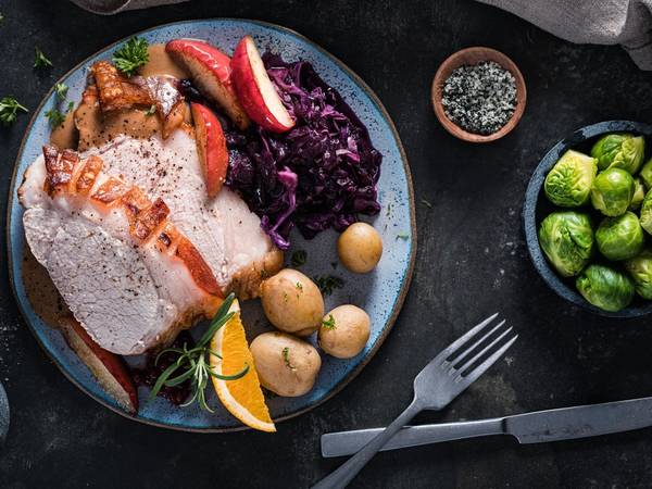 Skinkestek med tilbehør på tallerken, omgitt av grønnsaker og en liten skål med brune kuler