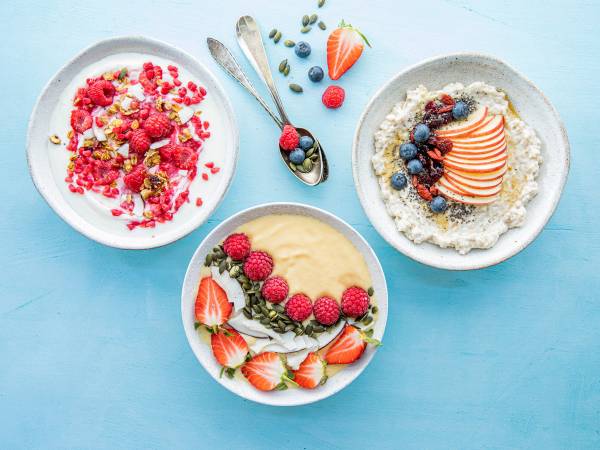 Tre skåler med smoothie bowls pyntet med bær og frukt på en blå bakgrunn