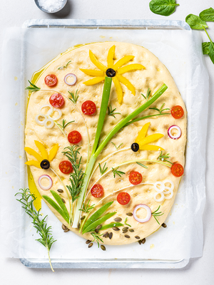 Focaccia med blomsterdekorasjon laget av grønnsaker og urter, formet som en blomstereng.