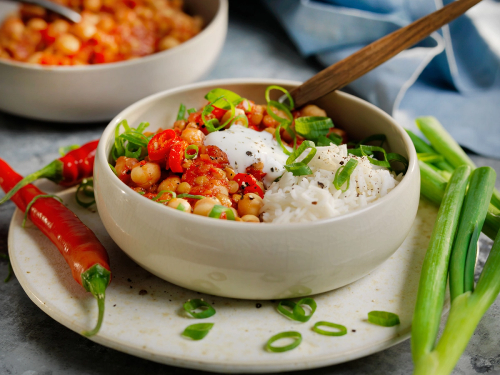 En bol med chili sin carne med grønnsaker og ris, pyntet med vårløk og servert med chili og selleristenger ved siden av.