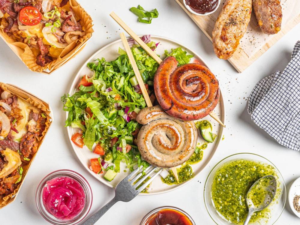 En tallerken med to store kjøttboller på spyd, omgitt av en grønn salat, med ulike småretter og sauser rundt på bordet.