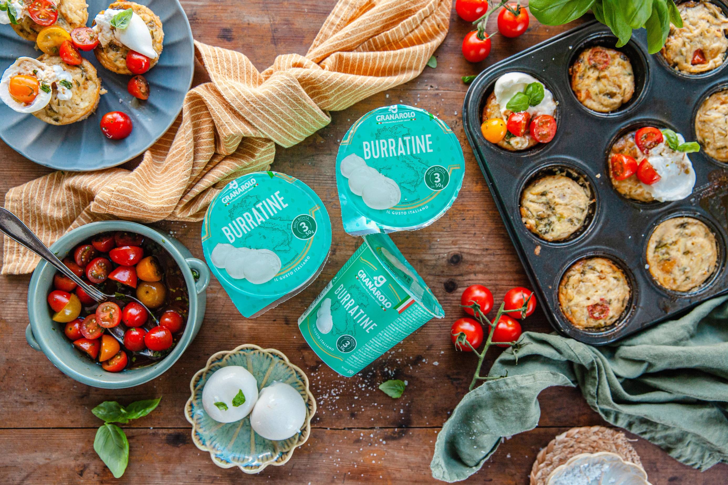 Muffins med jordbær og sitron, en skål med cherrytomater, og burattine-tyggegummi på et trebord med kjøkkenhåndklær