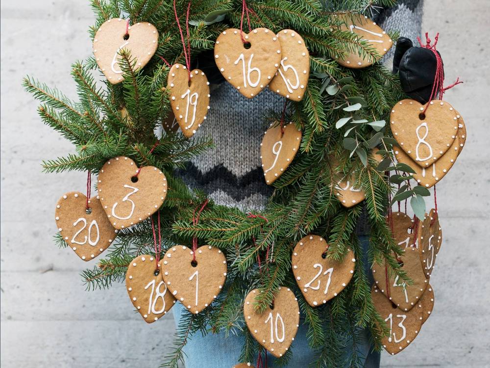 Pepperkakekalender med hjerteformede kalenderelementer med tall, hengende på en granbusk, brukt som julekalender.