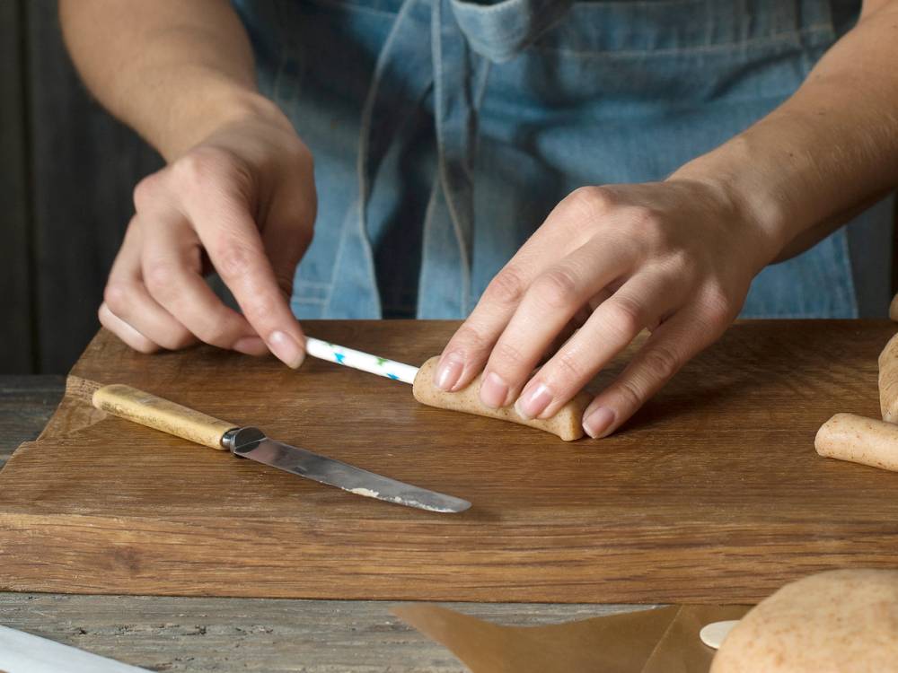 Person som jobber med å lage kransekakestang på et kjøkkenbord med et kniv og en skje ved siden av.