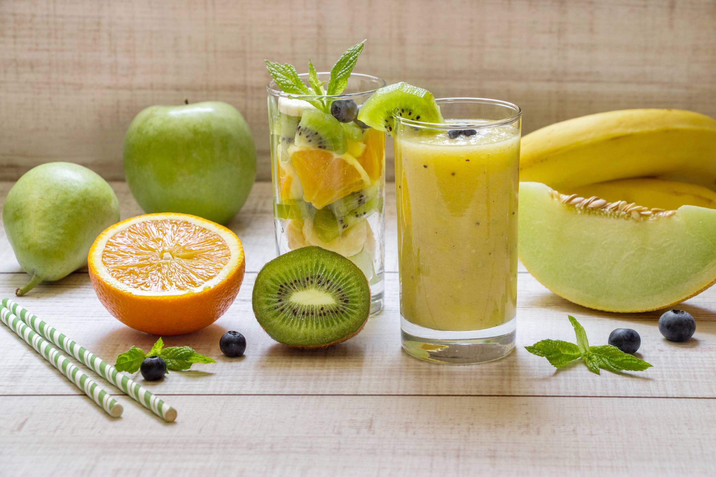 Et utvalg av frukt og en glass smoothie med sitron, kiwi, banan, og mynte på et lyst bord.