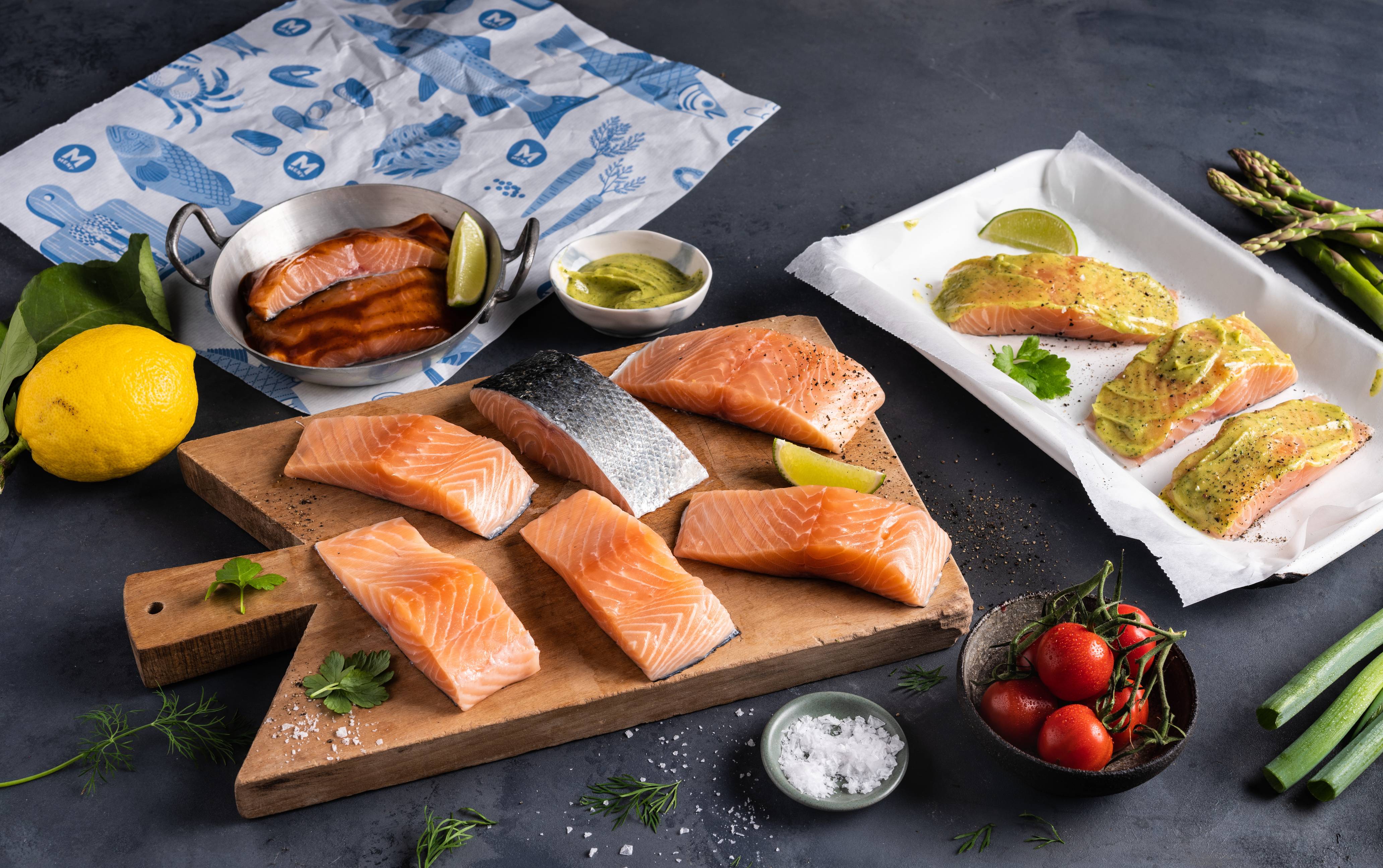 Lakseporsjoner med sitron, grønne asparges og cherrytomater på et kjøkkenbord, klar for grilling eller servering.