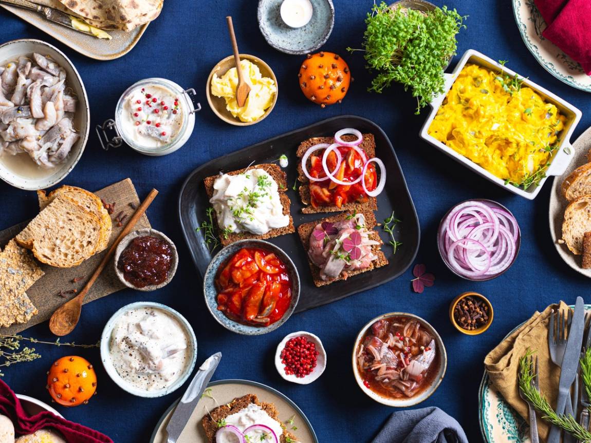 Et julebord med ulike retter og tilbehør, inkludert sild, på et blått bord.