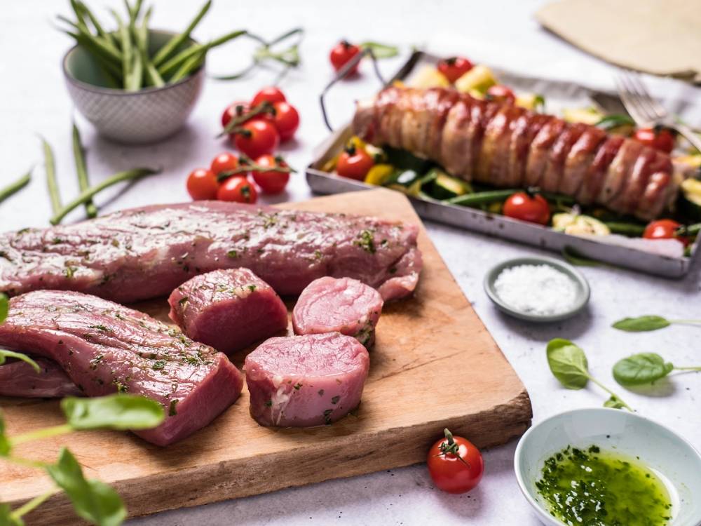 Svin indrefilet skåret i skiver på et skjærebrett med cherrytomater og urter rundt omkring.