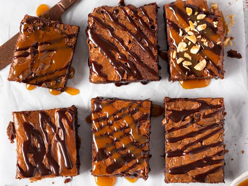 Seks fudgebrownies med sjokoladeglasur og nøtter på toppen, lagt ut på et hvitt underlag.