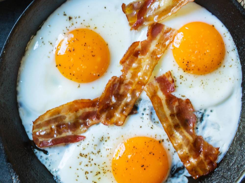 Tre stekte egg med sprøtt bacon i en panne.
