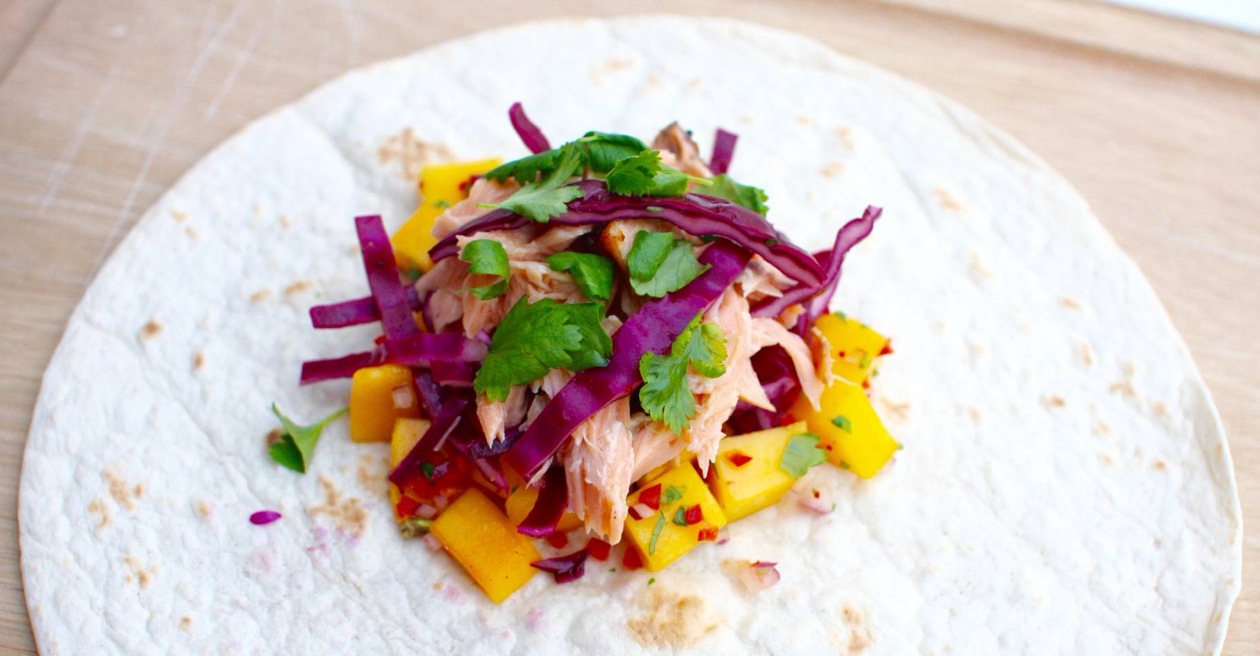 Troll Salmon mat med laks, mango, rødløk og koriander på en hvit tortilla, klar til servering.